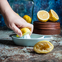 Hand squeezing a cut lemon, surrounded by lemons