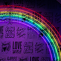 Neon sign of a rainbow in front of a wall covered in writing about love